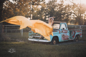 Flying dress in win while women models on old gmc pick up truck during photo session