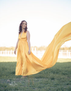 Model standing with long yellow dress in field during photo session